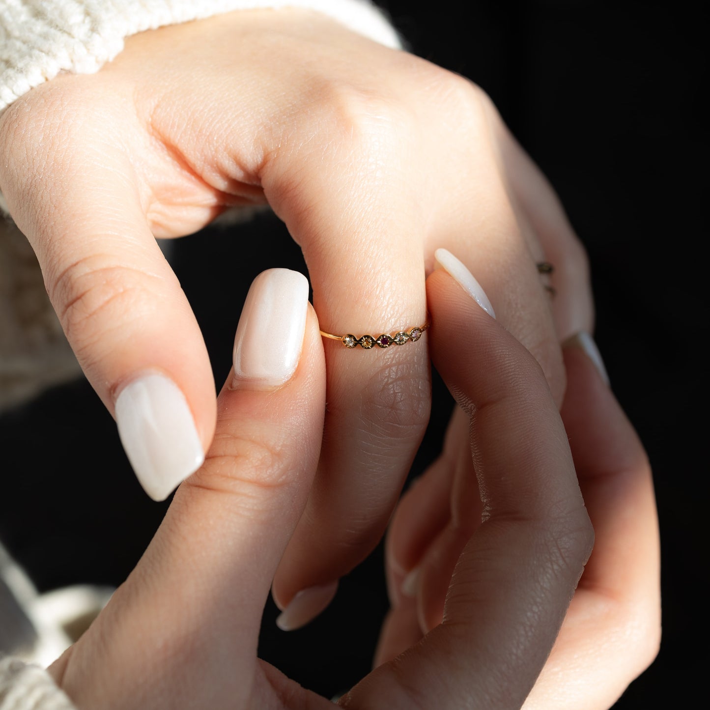 Close-up of a hand wearing a gold ring with small stones on a dark background