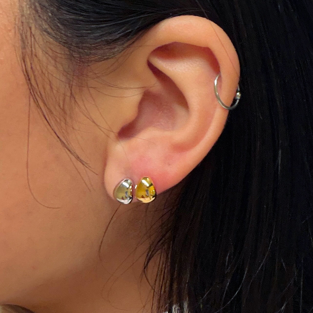 Close-up of an ear wearing gold teardrop earrings with a blurred background