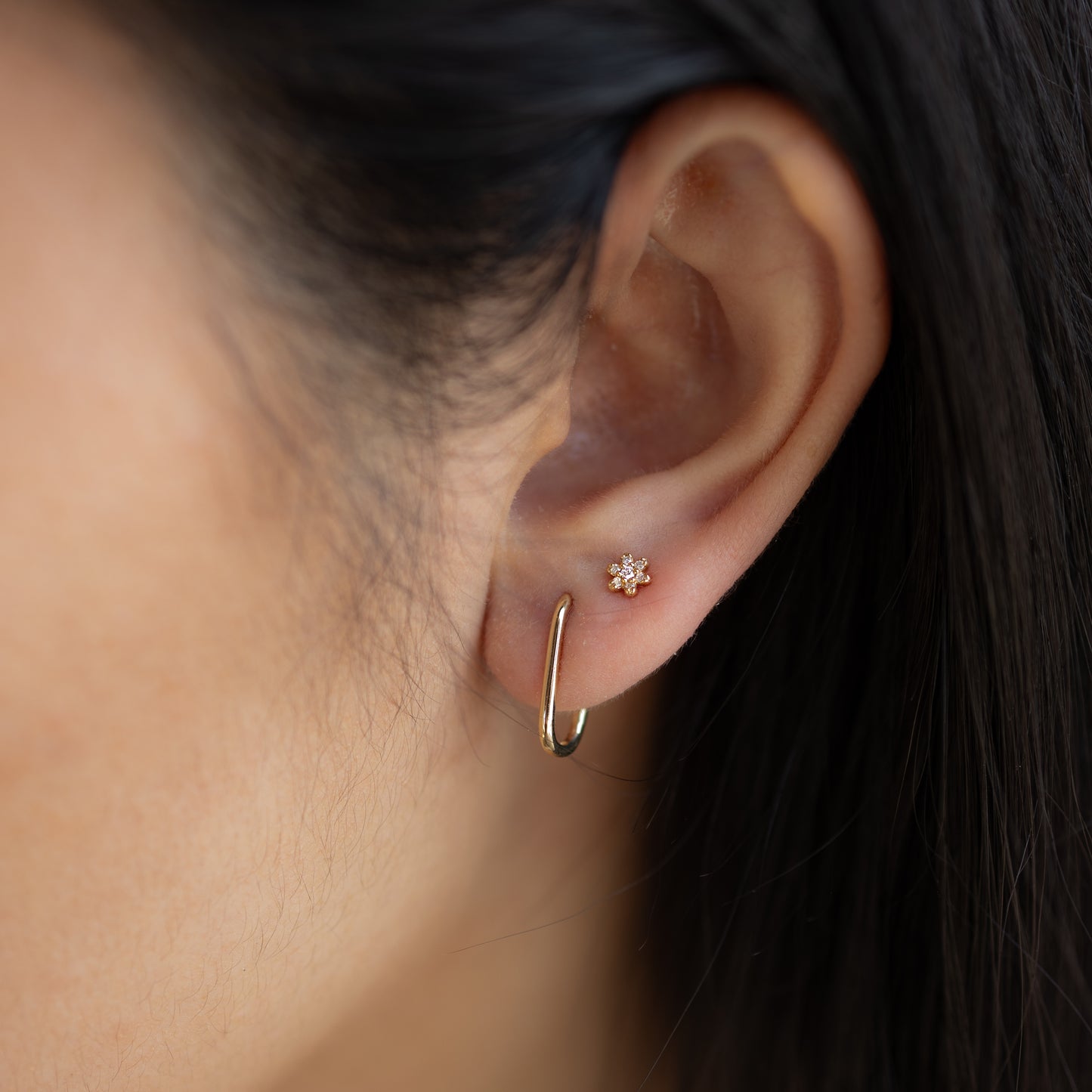 Close-up of an ear wearing gold hoop earrings with a star-shaped stud.