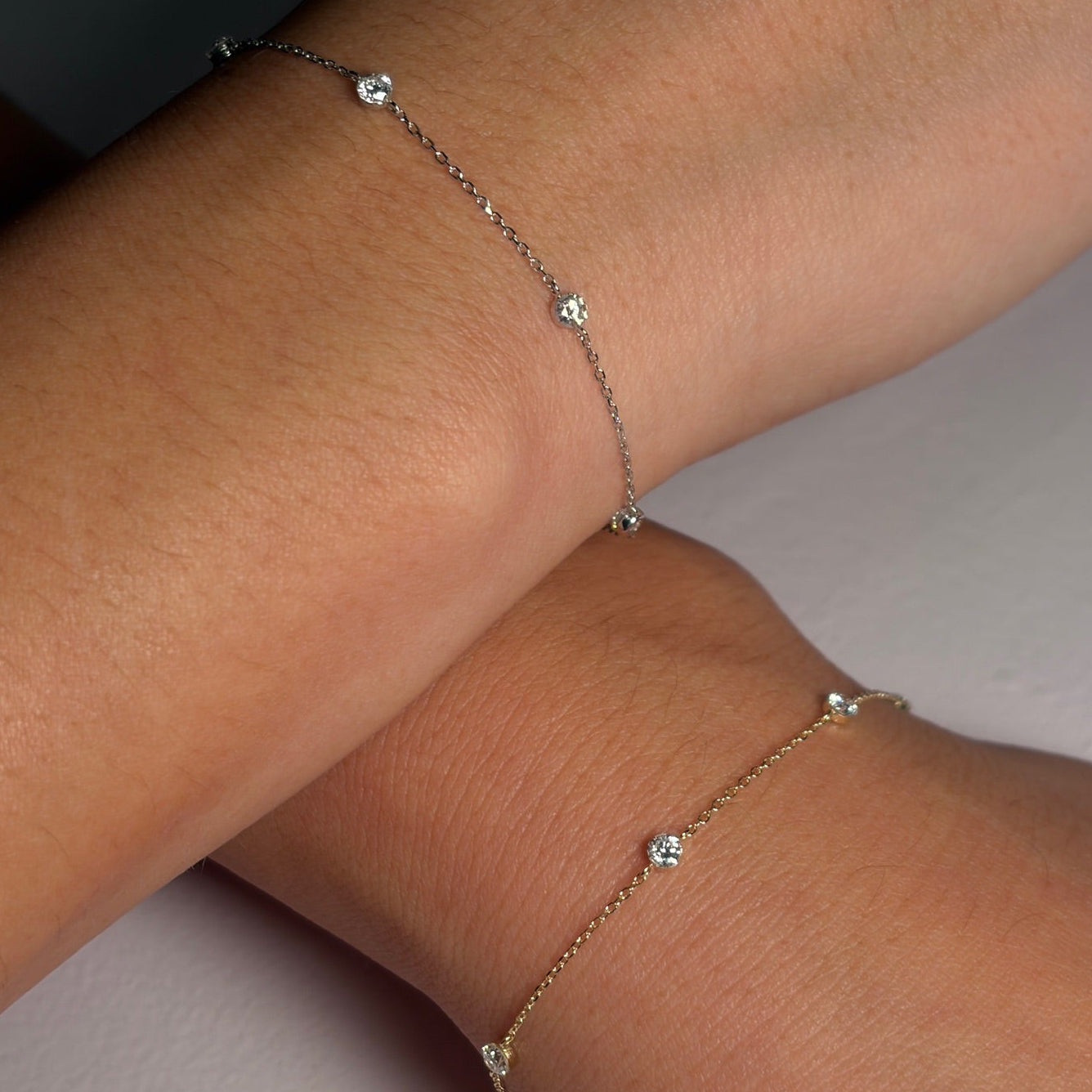 Close-up of a person's wrist wearing a delicate bracelet with small stones on a neutral background