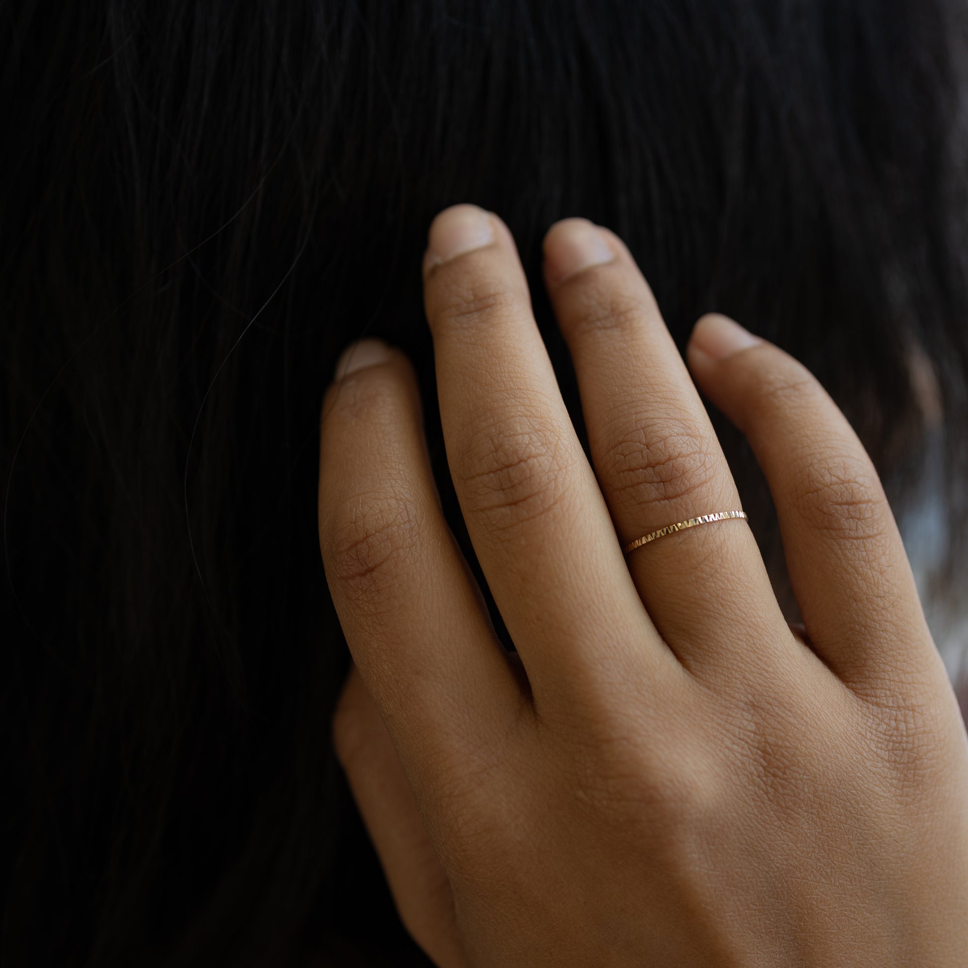 Hand wearing a gold ring on a dark background