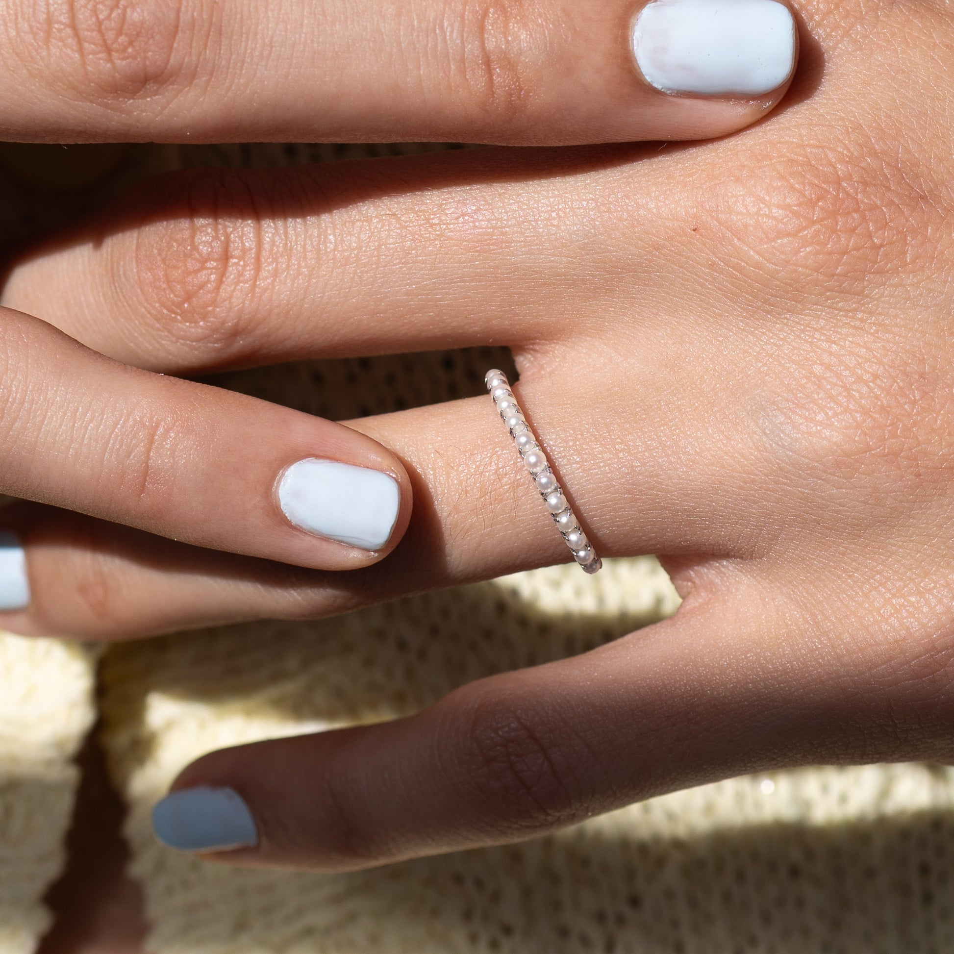 Close-up of a hand wearing a diamond ring with light blue nail polish.