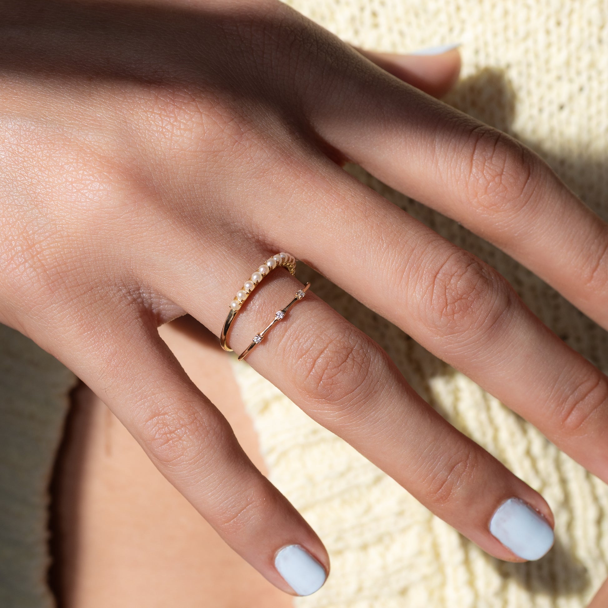 Close-up of a hand wearing two gold rings with a light background