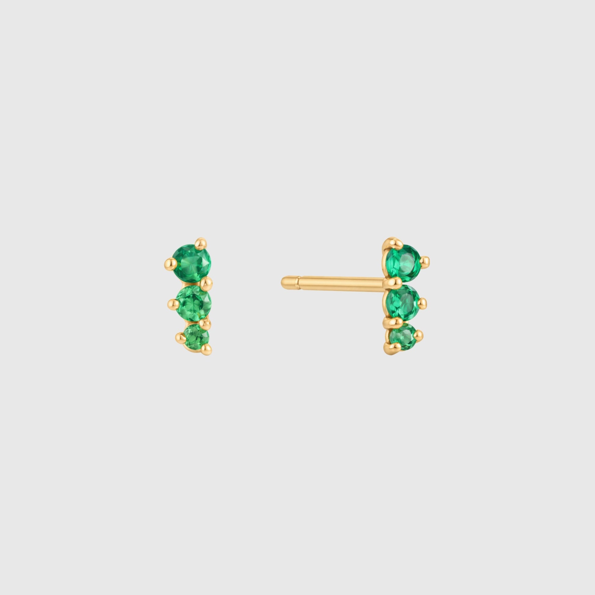 Gold earrings with green gemstones on a light gray background