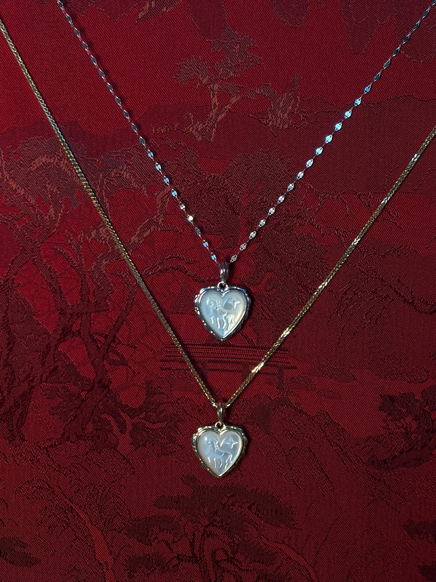 Two heart-shaped pendants on gold chains against a red lace background
