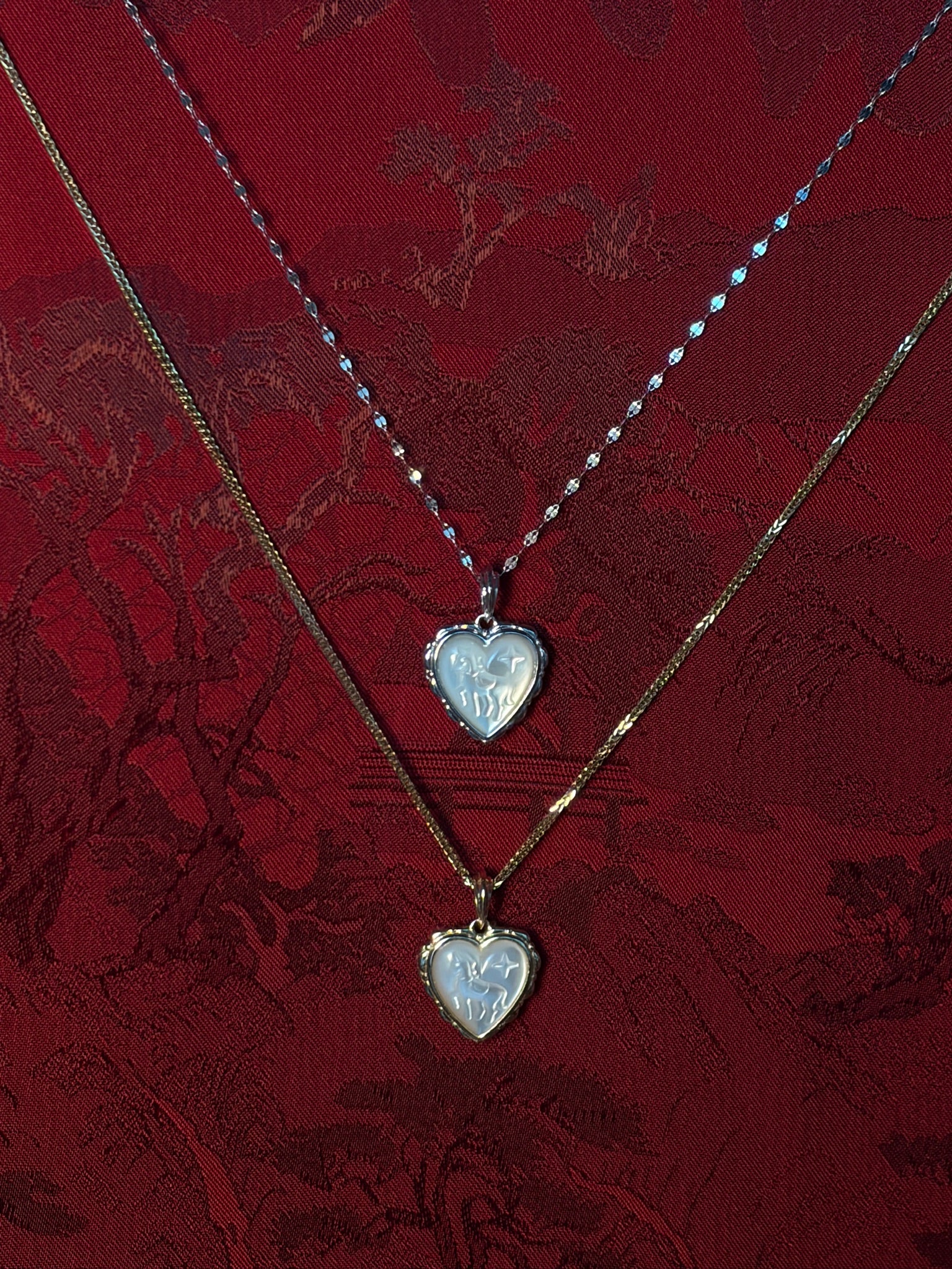Two heart-shaped pendants on gold chains against a red lace background