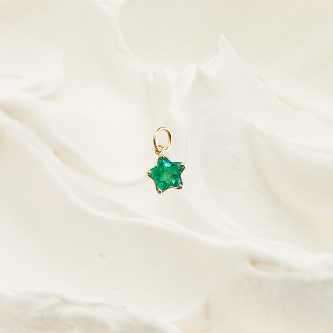 A small gold star-shaped pendant with a green faceted gemstone, resting on a soft, textured white fabric background.