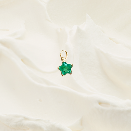 A small gold star-shaped pendant with a green faceted gemstone, resting on a soft, textured white fabric background.