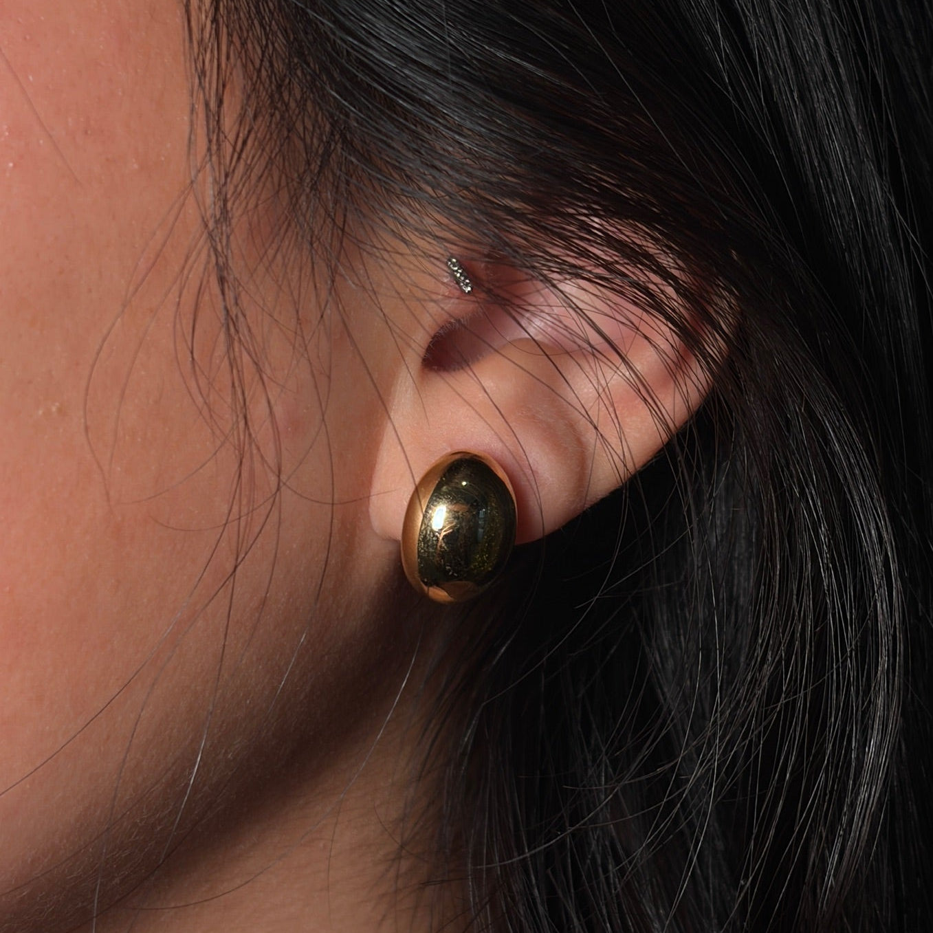 Close-up of a person wearing a gold earring with dark hair.