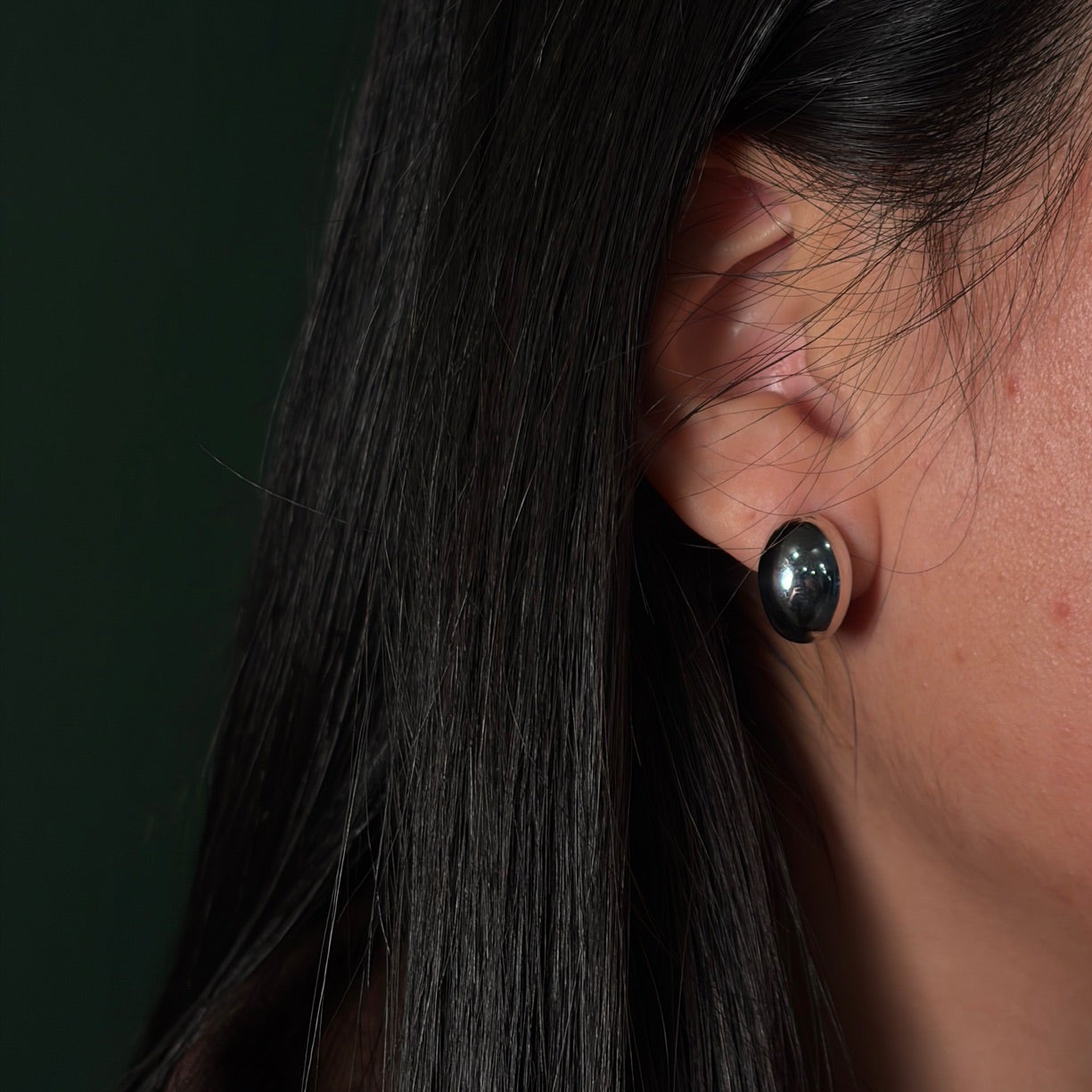 Close-up of an ear wearing a black earring with dark hair and skin.
